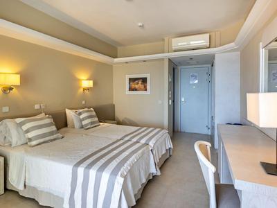 Chambre d'hôtel lumineuse avec deux lits, bureau et lampes murales chaleureuses.