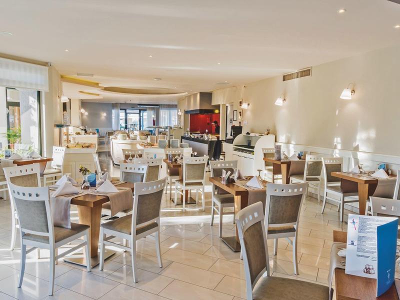 Bright hotel restaurant with wooden tables, chairs, and beige tiled floor