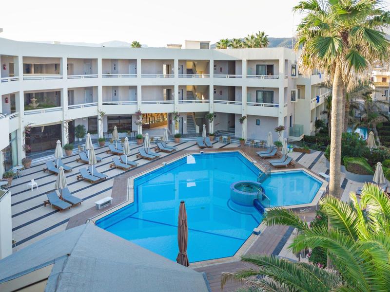 Hotel with a large outdoor pool surrounded by sun loungers and palm trees.