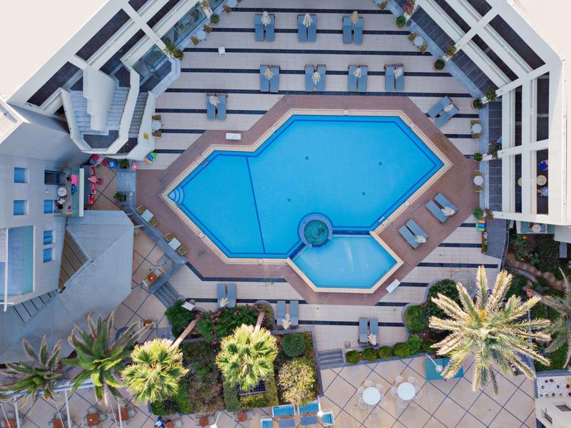 Top-down view of a hotel pool surrounded by sun loungers and palm trees.
