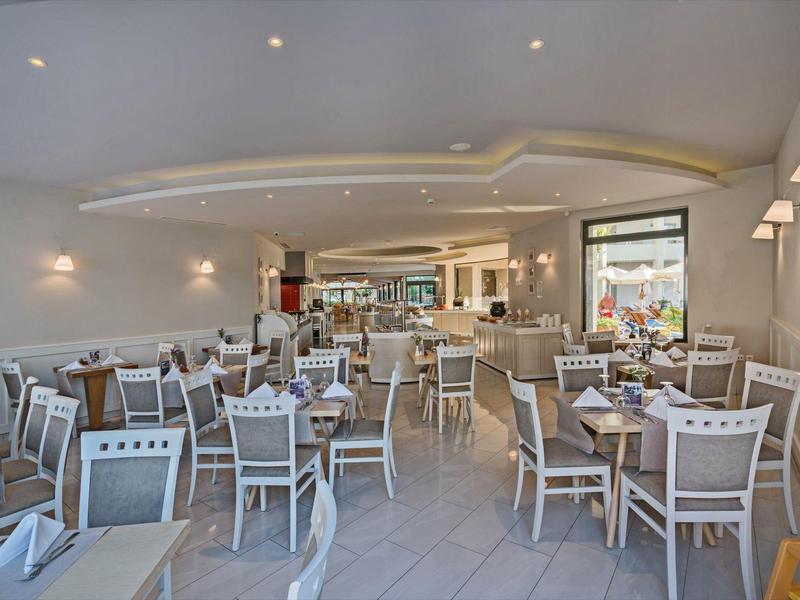 Spacious hotel dining area with white wooden chairs, tables set, and soft lighting.