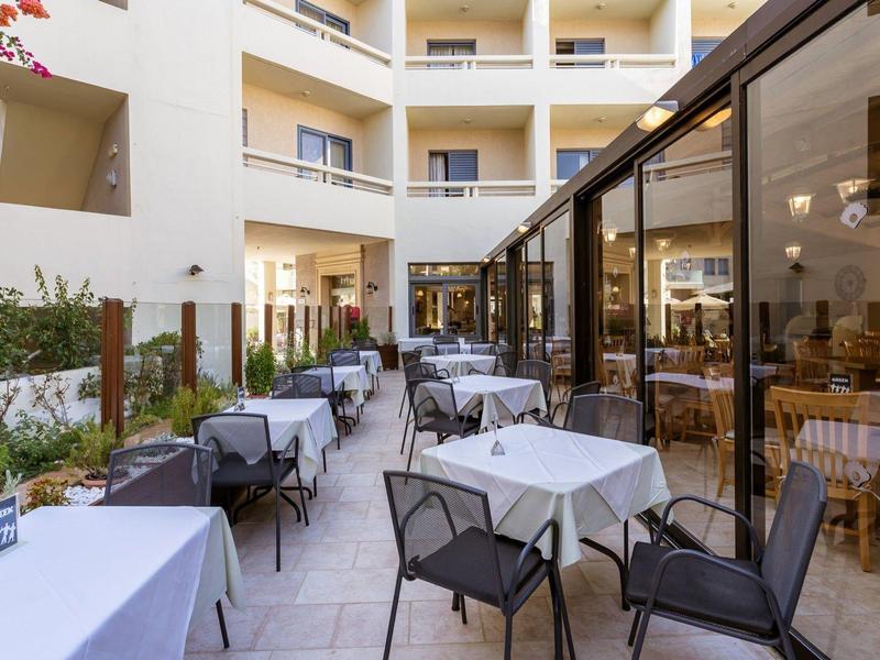 Outdoor hotel dining area with tables, chairs, and glass-enclosed indoor seating space.