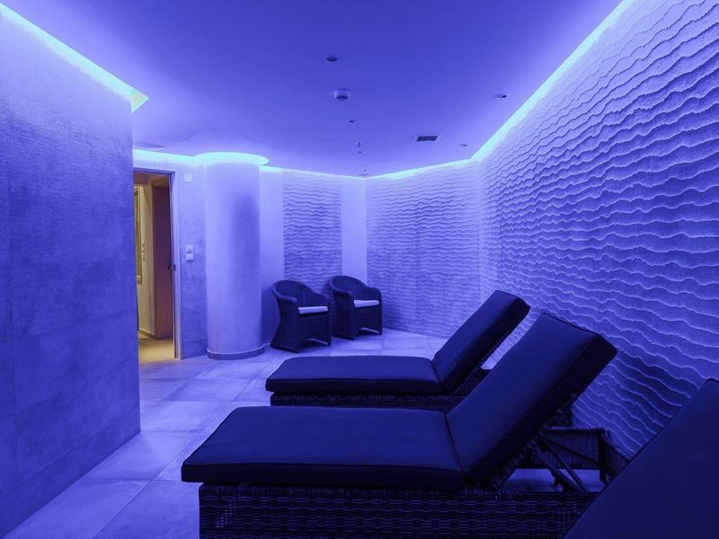 Relaxing spa room with lounge chairs and textured walls lit by blue LED lights.