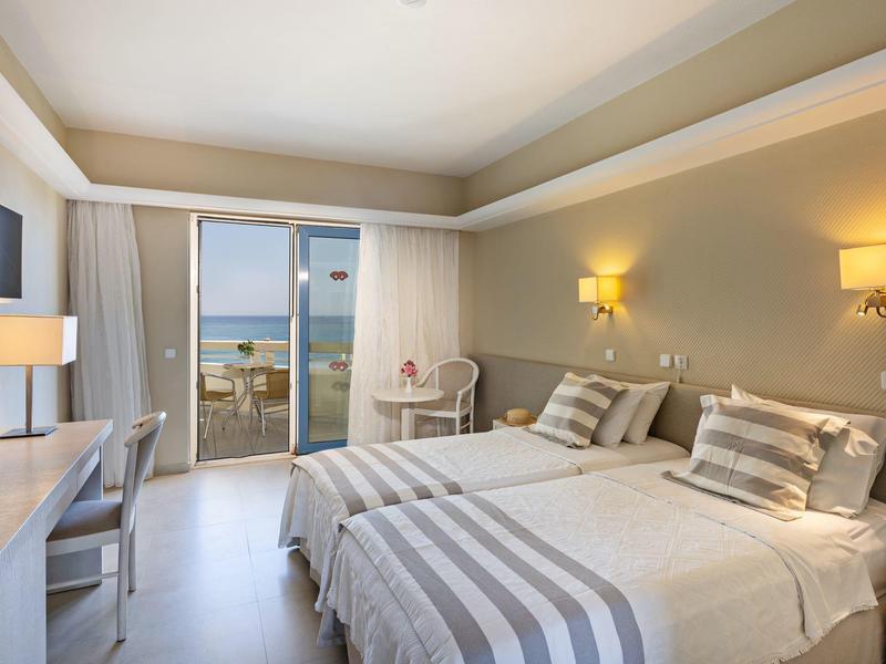 Modern hotel room with two twin beds, gray striped bedding, and balcony with ocean view.