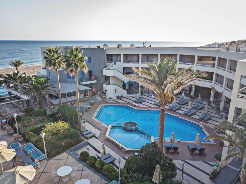 Hotel with outdoor pool, palm trees, sun loungers, near the beach with ocean view.