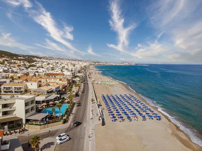 Zonnig strand met parasols, nabijgelegen stad, hotels en helderblauwe zee onder een heldere lucht.