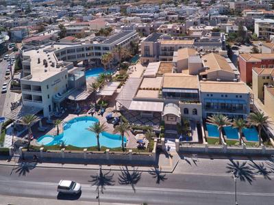 Luchtfoto van een groot hotelcomplex met zwembaden en palmbomen bij een drukke straat.