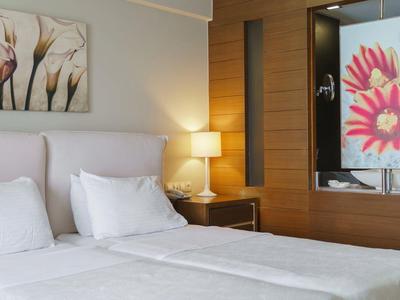 Moderne hotelkamer met tweepersoonsbed, wit beddengoed, nachtlampje en bloemenkunst.