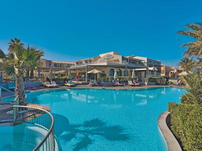 Duży basen przed ośrodkiem wypoczynkowym pod czystym niebem i palmami.