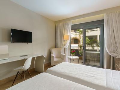 Habitación de hotel luminosa con dos camas, televisor, escritorio y balcón con vista a la piscina.