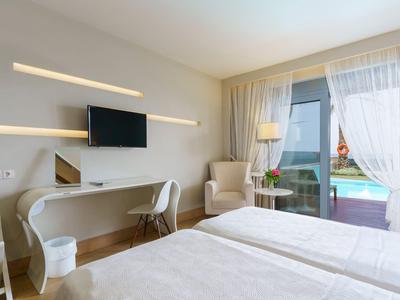 Habitación de hotel luminosa con dos camas, escritorio, silla y balcón con vista a la piscina.