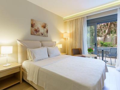 Habitación de hotel luminosa con cama doble, lámparas de noche y balcón con vista a la vegetación.