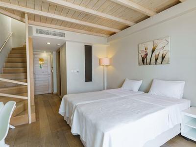 Habitación de hotel luminosa con dos camas individuales, techo de madera y escaleras al piso superior.