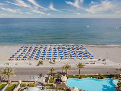 Strand met georganiseerde rijen blauwe parasols en een zwembad aan de overkant van de weg