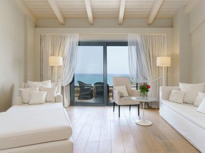 Lichte, moderne woonkamer met witte banken, houten vloer en balkon met zeezicht.