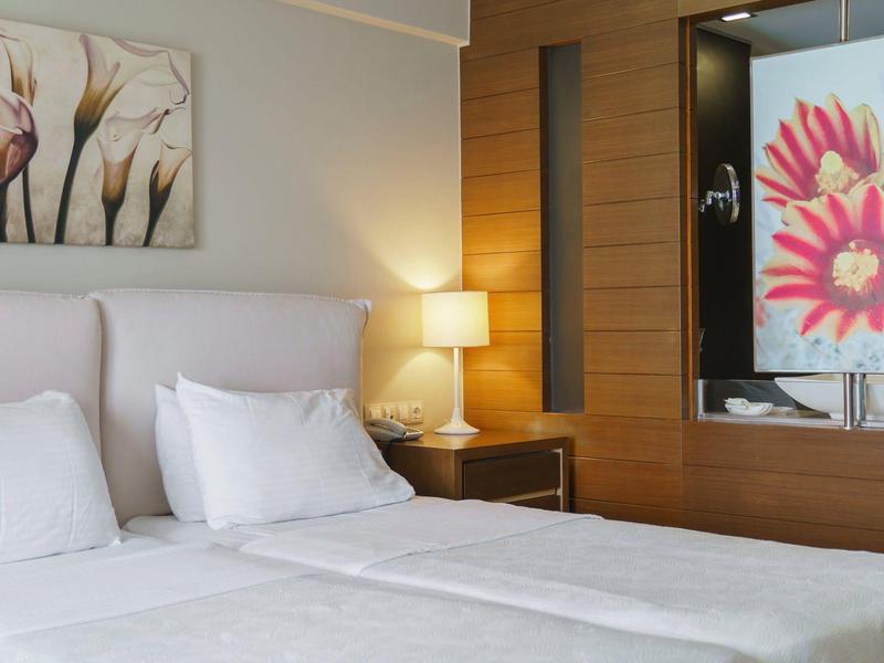 Moderne hotelkamer met tweepersoonsbed, wit beddengoed, nachtlampje en bloemenkunst.