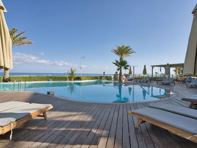 Rustig buitenzwembad met ligbedden en parasols met uitzicht op de oceaan onder een heldere lucht.