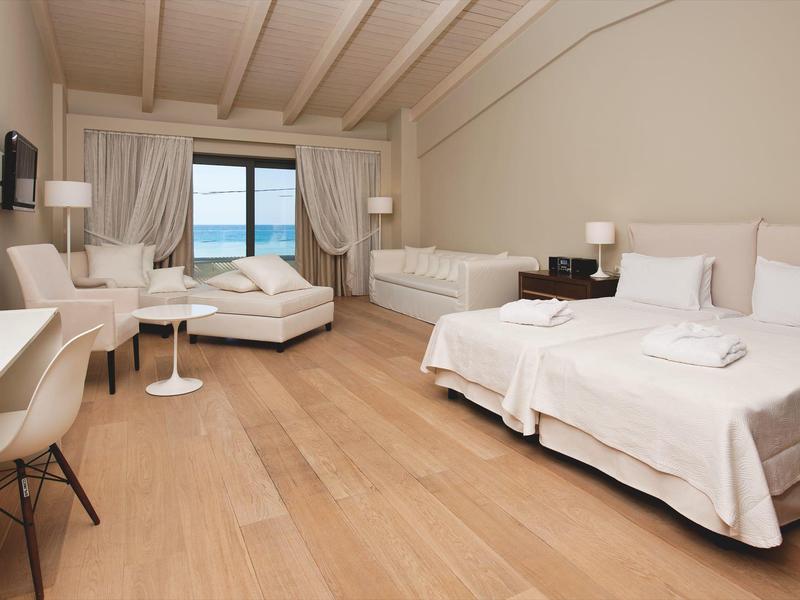 Lichte hotelkamer met twee bedden, houten vloer, wit meubilair en uitzicht op zee.