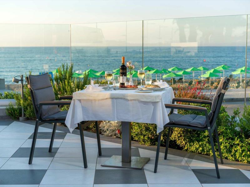 Buitentafel met wijn en eten met uitzicht op de oceaan en groene strandparaplu's.