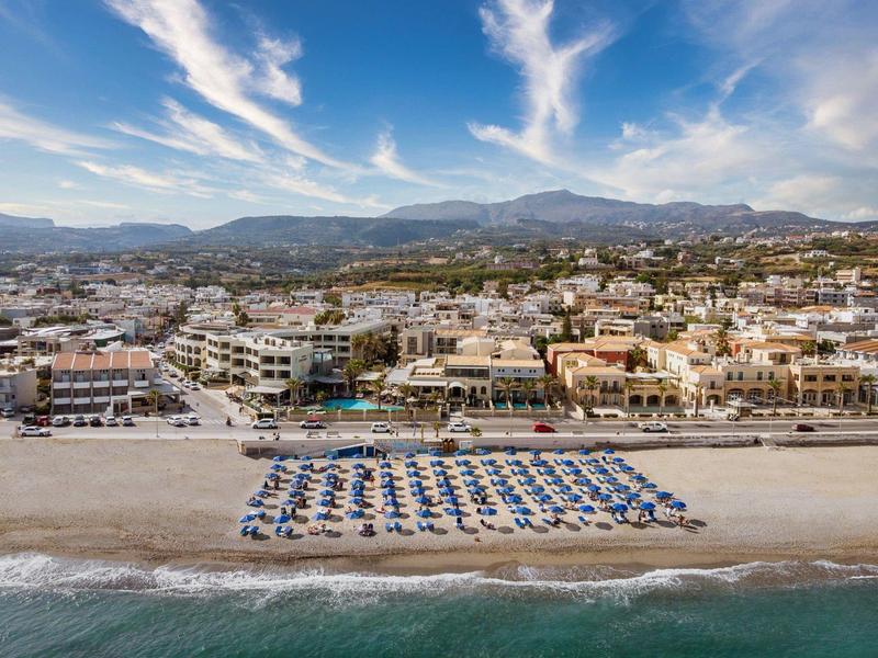 Strandstad met rijen blauwe parasols en ligbedden aan zee onder een deels bewolkte hemel.