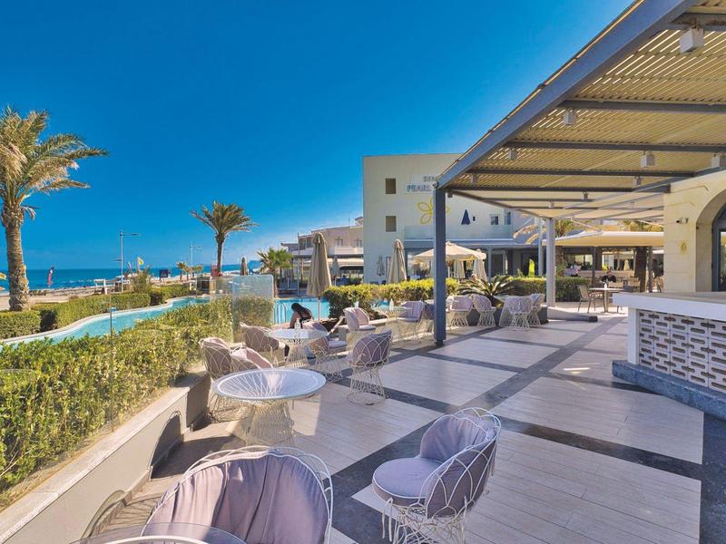 Buitenzitgedeelte bij een strandhotel met modern meubilair en heldere blauwe lucht.