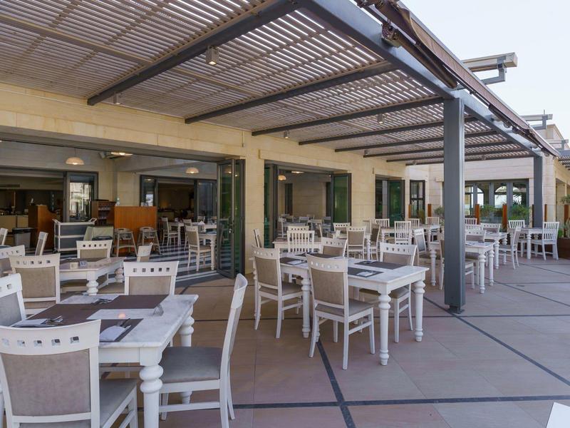 Ruim buitenterras met witte stoelen en tafels onder een pergola.