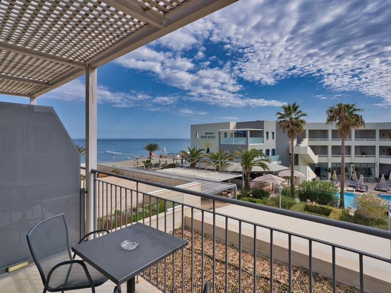 Uitzicht vanaf balkon van hotel met zwembad, palmbomen en oceaan onder deels bewolkte hemel.