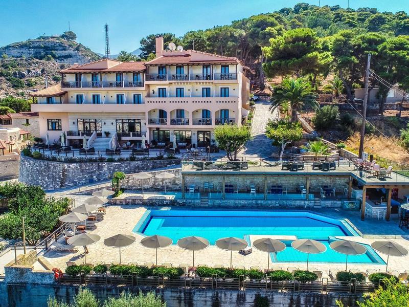 Hotel mit Außenpool, Sonnenschirmen und Pinien in hügeliger Landschaft.
