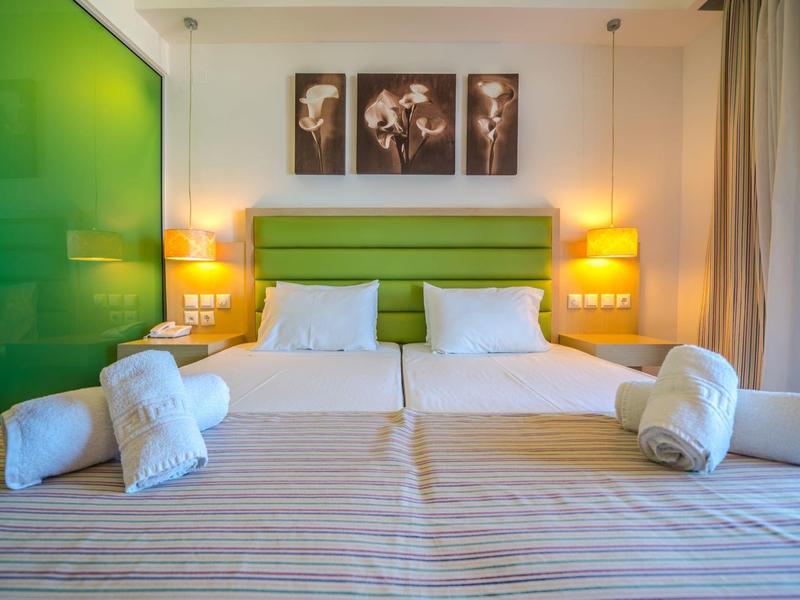 Modernes Hotelzimmer mit zwei Einzelbetten, grünem Kopfteil und stimmungsvoller Beleuchtung.