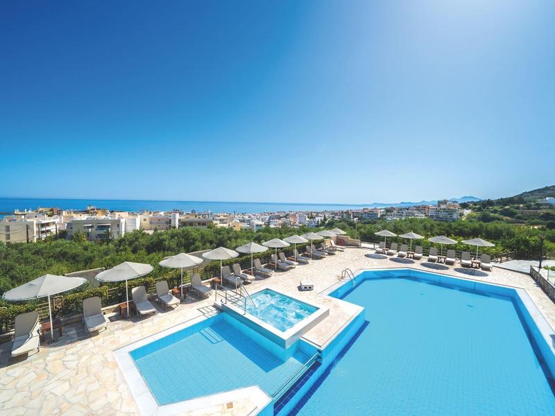 Hotelpool mit Sonnenliegen, Sonnenschirmen und Meerblick an einem sonnigen Tag.