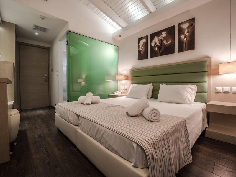 Modernes Hotelzimmer mit Doppelbett, grüner Wand, stilvollen Bildern und warmem Licht.