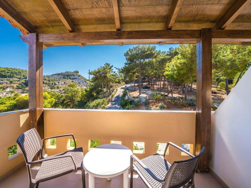 Balkon mit Tisch und Stühlen unter einem Holzdach mit Blick auf grüne Hügel und Häuser.