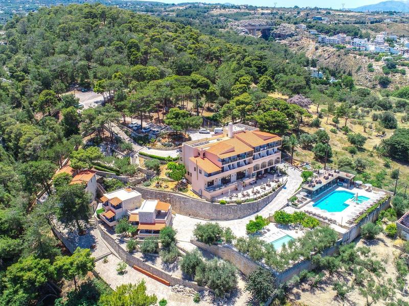 Luftaufnahme eines Hotels inmitten von viel Grün mit Swimmingpool und umliegenden Bergen.