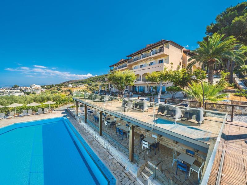 Hotel mit Terrasse, Pool und Blick auf Landschaft unter blauem Himmel.