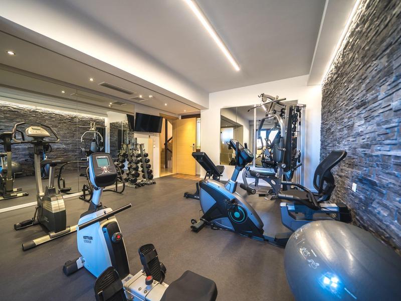 Modernes Fitnessstudio mit Trainingsgeräten und Steinwand im Hotelbereich.