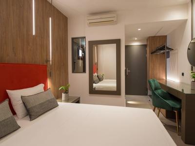 Modernes Schlafzimmer mit großem Bett, roten Akzenten, Holzvertäfelung und grünem Sitzbereich.