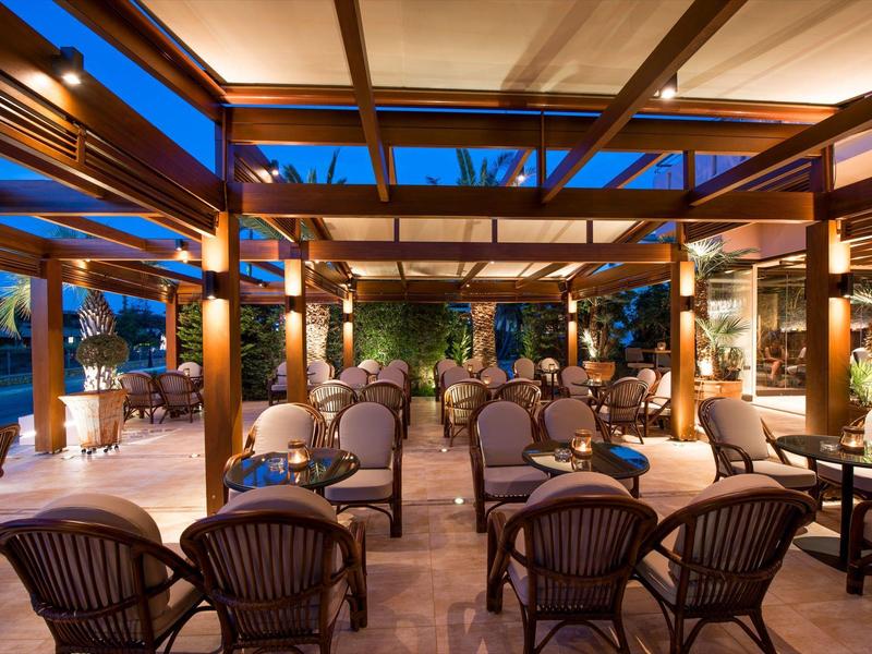 Gezellig overdekt buitenterras van een hotel met tafels en stoelen bij schemering.