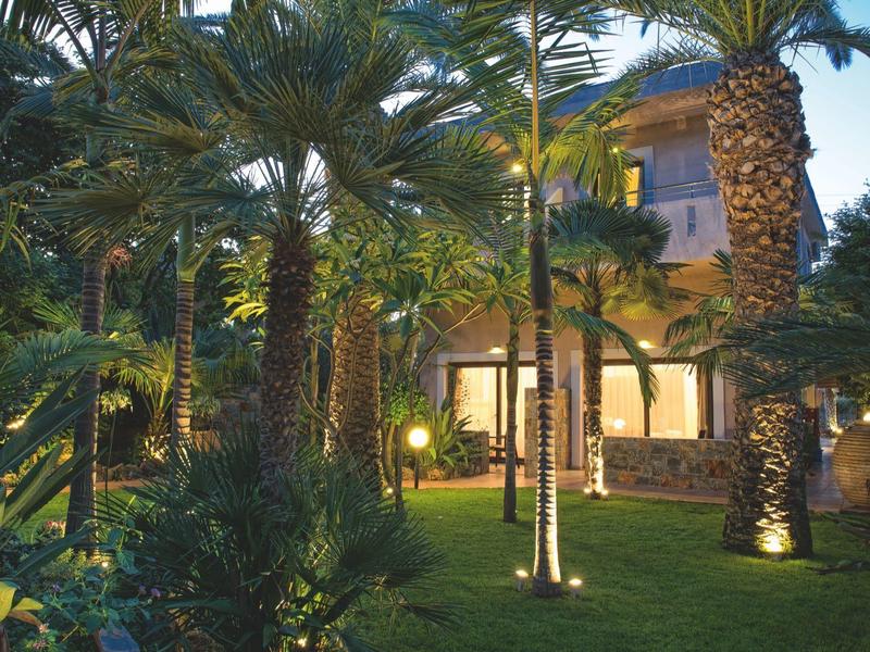 Verlichte tuin met palmbomen en hotelgebouw op de achtergrond bij schemering.