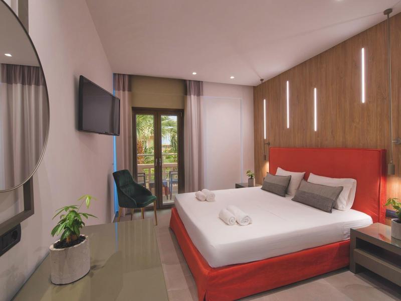 Modern hotelkamer met groot bed, houten accentmuur en balkon met uitzicht op groen.