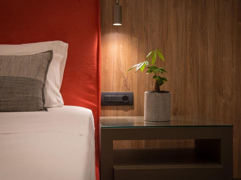 Moderne slaapkamer met wit bed, houten nachtkastje en kleine plant in een grijze pot.