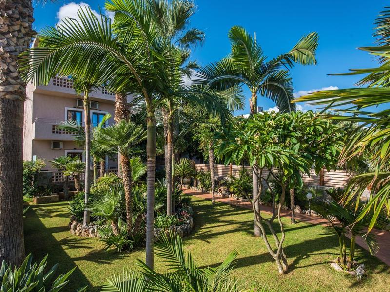 Weelderige tuin met palmbomen voor een meer verdiepingen tellend hotel onder een heldere blauwe lucht