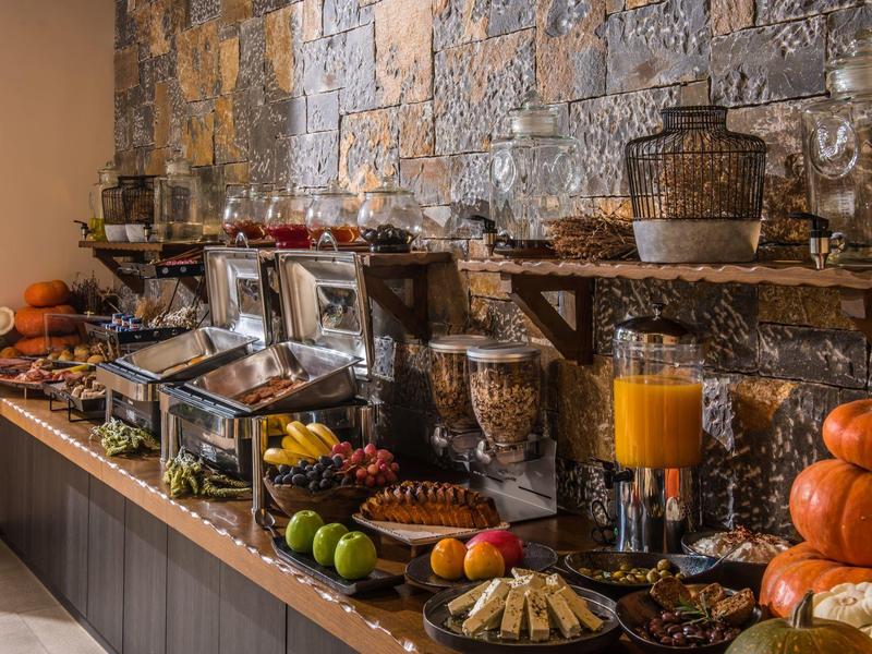 Buffet met verschillende gerechten, fruit, sap en decoratieve pompoenen tegen een stenen muur.