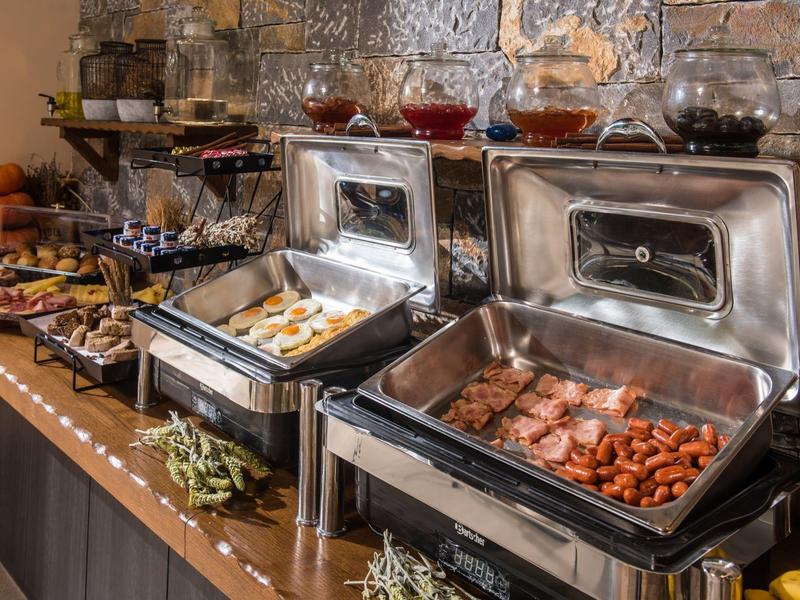 Buffet met diverse warme gerechten in verwarmde roestvrijstalen containers op een houten toonbank.