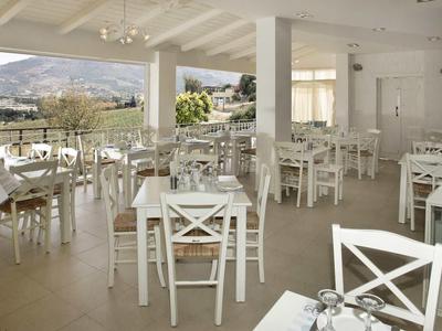 Helles Restaurant mit weißen Stühlen, Tischen, großen Fenstern und Blick auf Berge im Hintergrund.