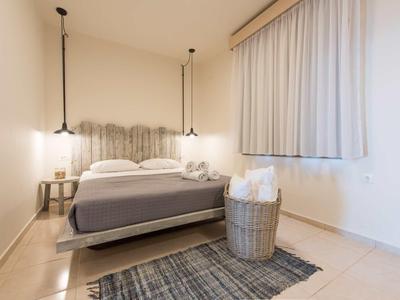 Jednoduchý hotelový pokoj s manželskou postelí, kobercem, košem s ručníky a dvěma závěsnými světly.