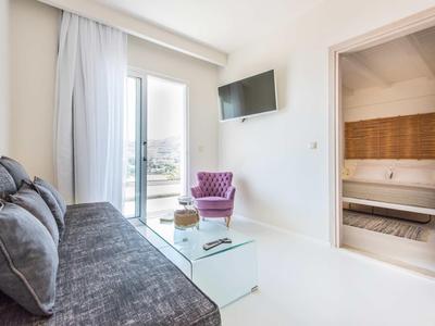 Soggiorno luminoso con divano grigio, poltrona viola, tavolino in vetro e TV a parete.