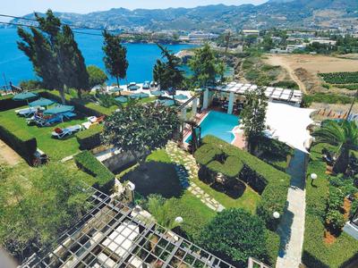 Pohled na zahradu s bazénem, lehátky a mořem s horami v pozadí.