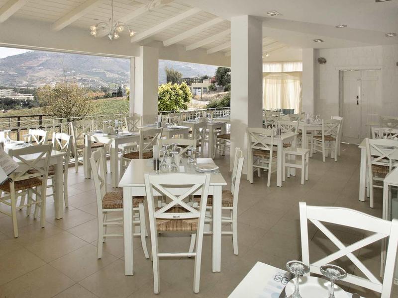 Otevřená jídelna s bílými dřevěnými stoly a židlemi, výhled na krajinu přes velká okna.