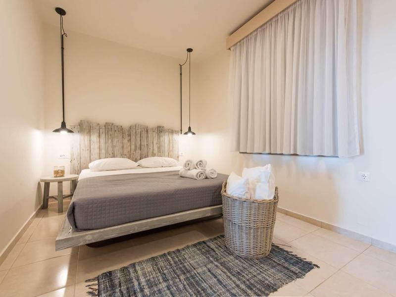 Jednoduchý hotelový pokoj s manželskou postelí, kobercem, košem s ručníky a dvěma závěsnými světly.