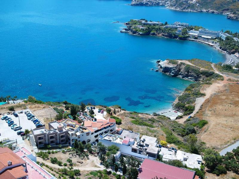 Letecký pohled na přímořský komplex s budovami, parkovištěm a čistým modrým mořem.